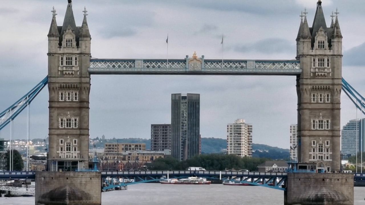 Tower Bridge seen front-on, its two stone towers and high walkways framing tower blocks behind