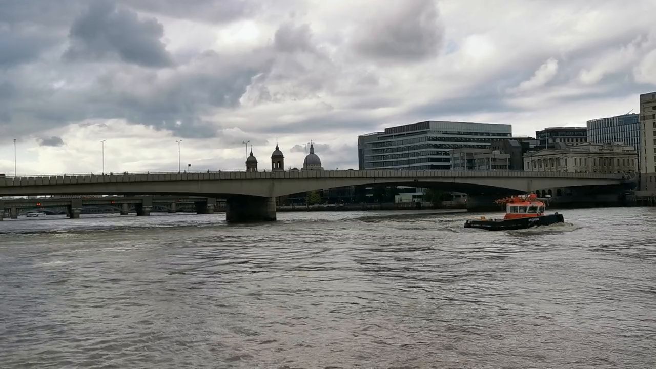 The long, low concrete spans of London Bridge across the Thames, with a small boat passing underneath