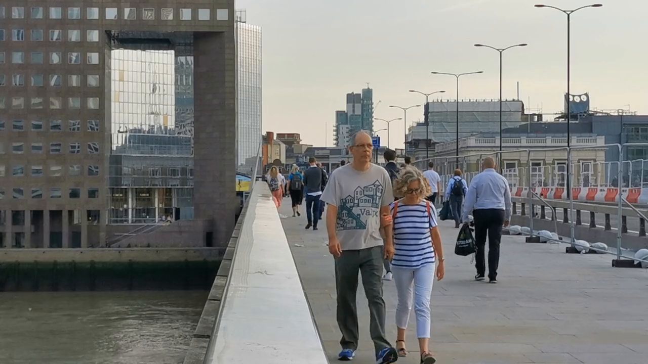 People walking along the pavement of London Bridge on a grey day, a large office building with a square opening ahead